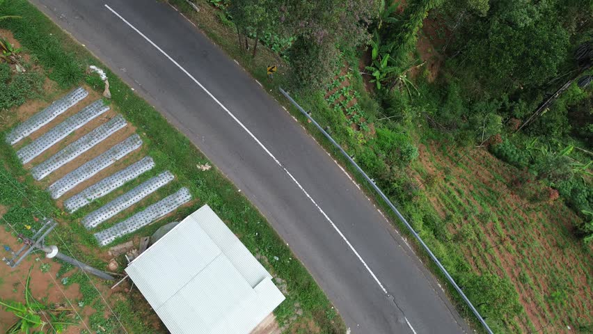 Top Down Aerial View of Winding Road with White Car and Motorcycle in Green Hills