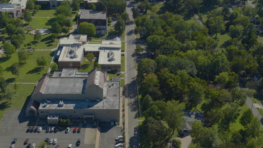 College campus buildings surrounded by green trees and lawns on a clear midday in Clarksville, Arkansas, aerial drone perspective.