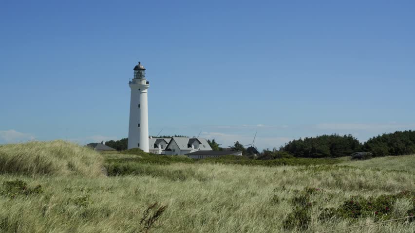 Picturesque white lighthouse standing on a grassy dune with the wind blowing through the grass