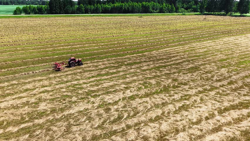 Tractor towing grass mower across harvested field with clear blue skies and vibrant green grass