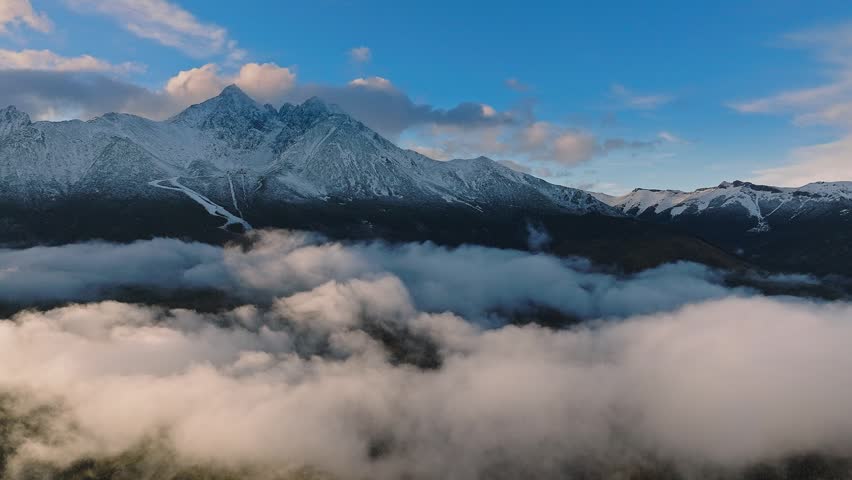 High Tatras, Slovakia - 4K flying by the High Tatras mountains above clouds on a foggy autumn day with blue sky and clouds