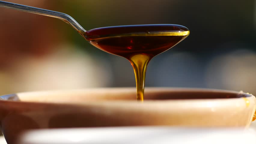 Thick honey cascades from a spoon into a rustic bowl, capturing sweetness.