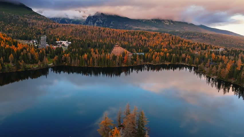Strbske Lake, Slovakia - 4K Flying above Strbske Lake (Strbske Pleso) on a sunny autumn afternoon at sunset with High Tatras at background. Blue water, warm colors, mountains covered with clouds