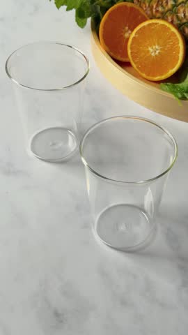 A vertical footage of pouring green smoothie in glass cup near fruits plate on marble table