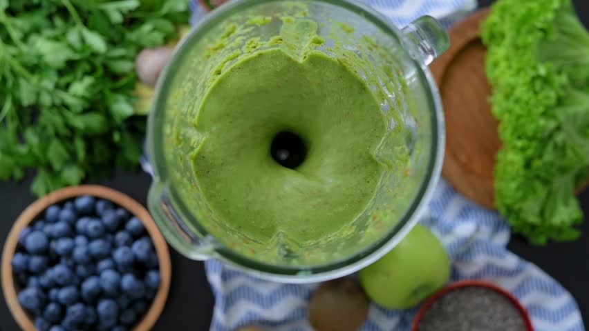 Green smoothie blending inside blender features fresh leafy ingredients viewed from above. Smoothie supports healthy nutrition, vibrant green drink suits wellness campaigns, diet concepts, lifestyle 