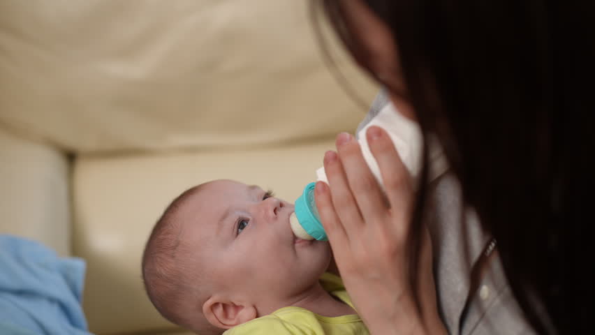 Caring young mother feeding her adorable infant son with a bottle of milk. A beautiful moment of bonding between a mom and her baby