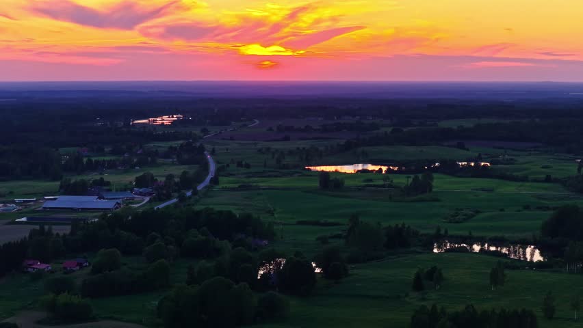 Aerial view of rural landscape with fields, ponds, and a vivid sunset sky overhead