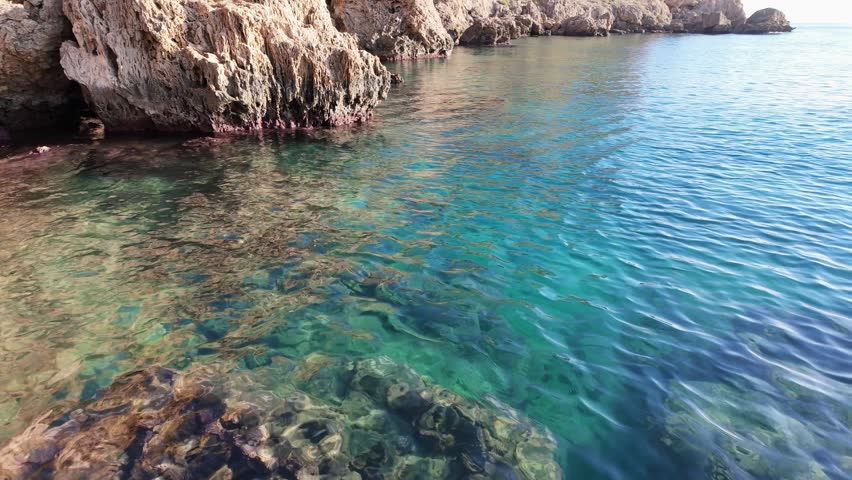 Clear turquoise mediterranean sea water rippling gently over a shallow rocky reef.
