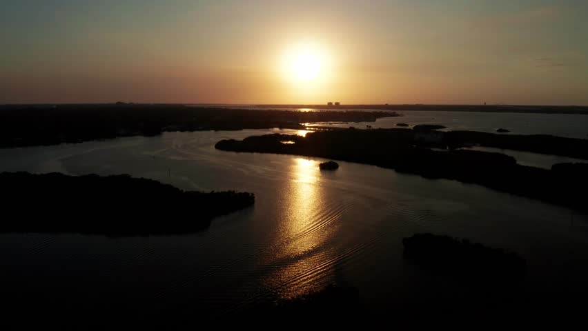 Low sun casts a bright path of light across a broad wetland lagoon as mangrove-covered islands form dark silhouettes in the distance.