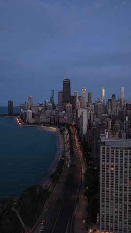Chicago skyline showing John Hancock Center and Oak Street Beach along Lake Shore Drive with urban traffic moving at blue hour, Gold Coast neighborhood, Illinois, USA