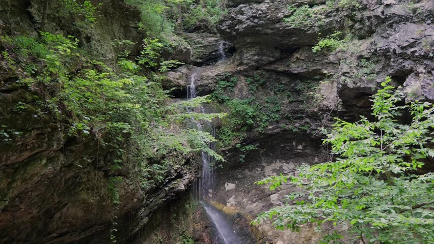 Scenic view of a natural waterfall cascading down a steep, mossy limestone rock bluff face deep inside a lush green Arkansas summer forest