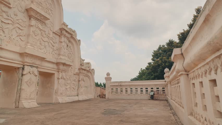 Ancient Javanese royal garden featuring ornate stone walls, intricate relief carvings, and traditional Indonesian architectural details under a cloudy sky in Yogyakarta.