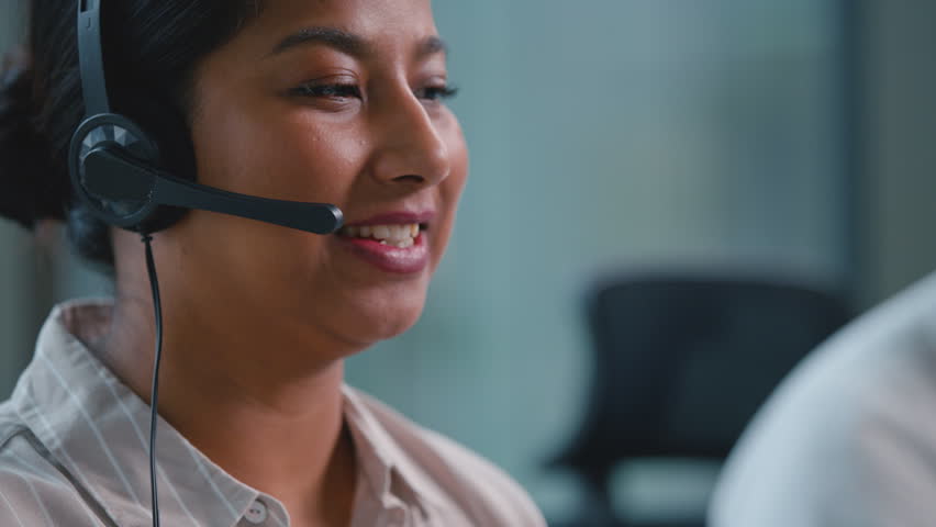 Close up smiling happy Arabian female receptionist talking in headset microphone Indian business woman ethnic joyful carefree businesswoman talk in call center operator consulting client in callcenter