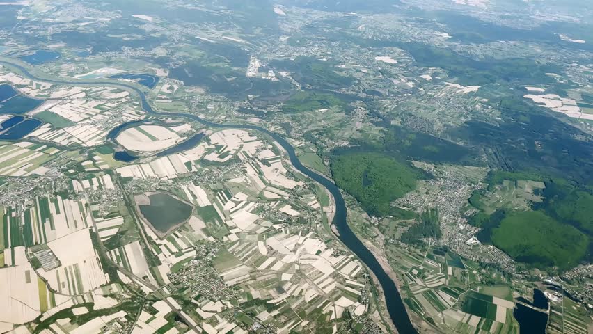 Aerial view of a winding river through farmland, forests and scattered towns, showing patchwork fields, reservoirs and broad countryside from above.