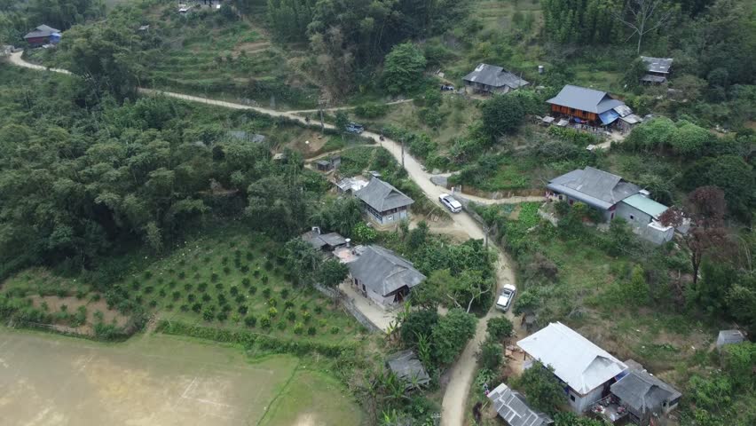 A high-angle view showing several dirt trails and pathways converging into a single main road, with small traditional houses and lush greenery scattered along both sides.