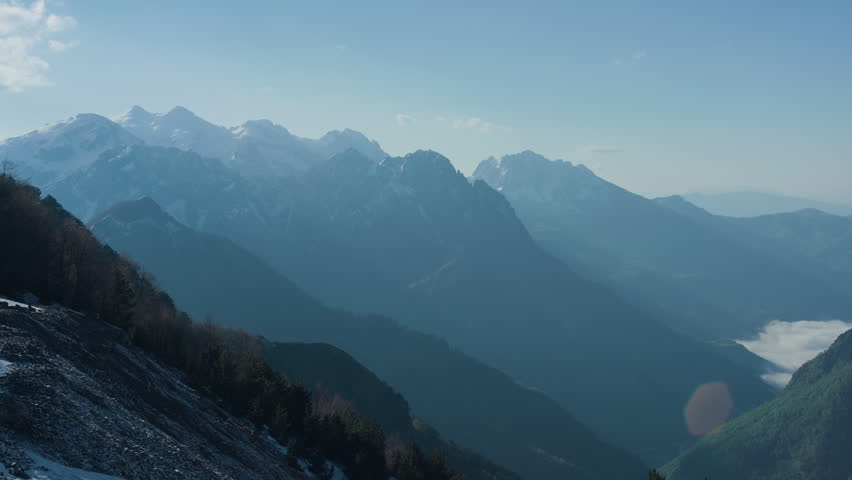 Snowy mountain valley green trees and rocky peaks, static tripod view. Winter alpine landscape with forest under a clear sunny blue sky.