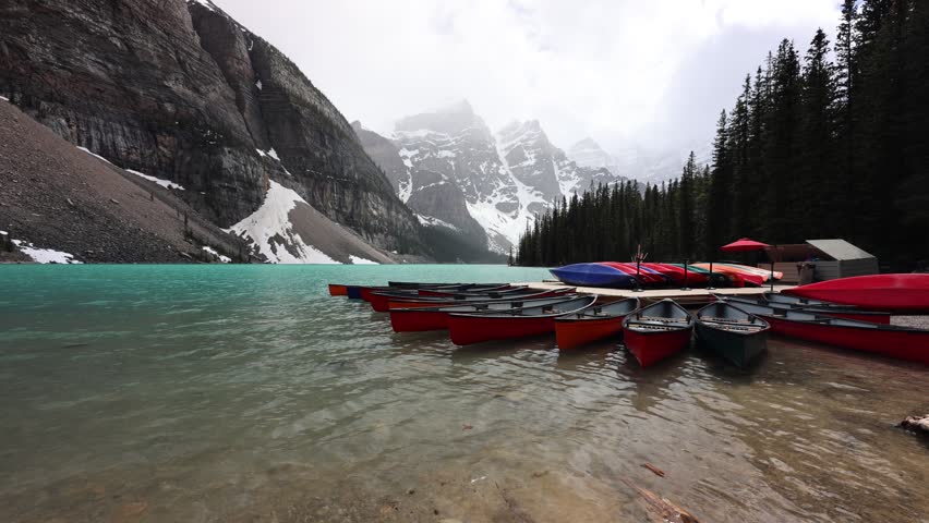 Stunning footage of Moraine Lake in Banff National Park showing crystal clear turquoise glacial waters surrounded by the majestic Rocky Mountains and dense pine forests in Alberta Canada