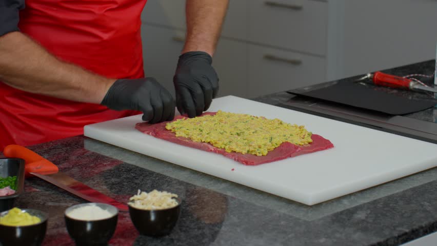 Close-up, chef rolling a stuffed meat preparation with savoury filling in a commercial kitchen. Suitable for food preparation, catering, restaurant, and culinary themes