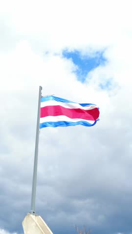 The official flag of costa rica fluttering on a flagpole against a cloudy sky