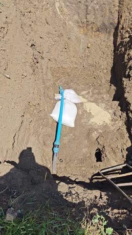 Repaired water pipeline section with sandbags for stabilization in a narrow open trench, outdoor construction.