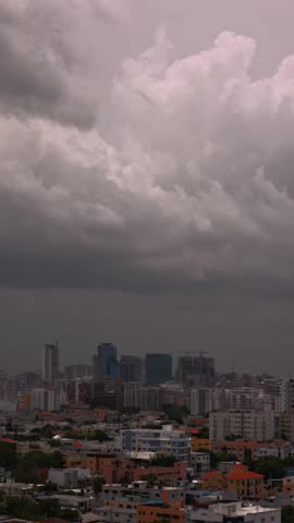 Dramatic dark storm clouds gathering over a dense Santo Domingo city skyline. Urban landscape under a moody, overcast sky before rainfall.