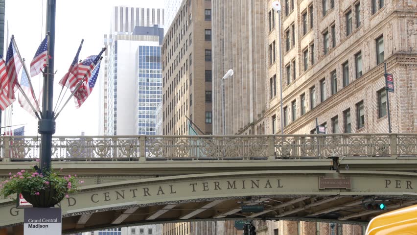 American flags near Grand Central Terminal on 42 street, New York City, Manhattan Midtown. Bridge to railway building, urban architecture in United States. Public railroad transport junction.