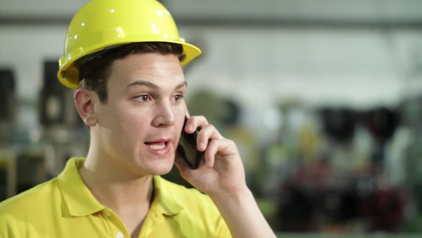 Contractor in hard hat on angry phone call in industrial setting.