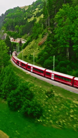 Aerial video of the red train traversing the Landwasser viaduct. The Swiss Express travels through the green meadows and mountains of Switzerland. Passenger transportation in Switzerland