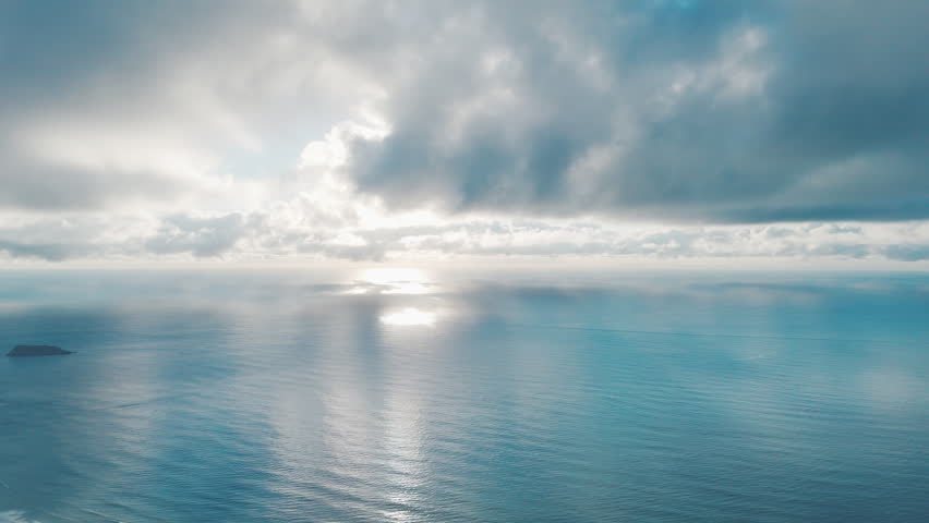 Aerial high altitude view of the Atlantic Ocean surface during calm sunrise with clouds running in the sky