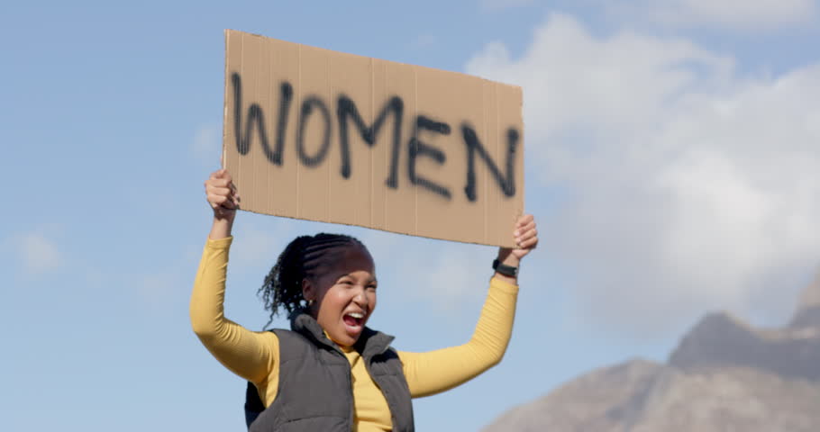 Raising cardboard WOMEN sign calling to get attention, woman in vest walking railing, copy space. Protest, advocacy, empowerment, visibility, mountains, overlook, outdoor