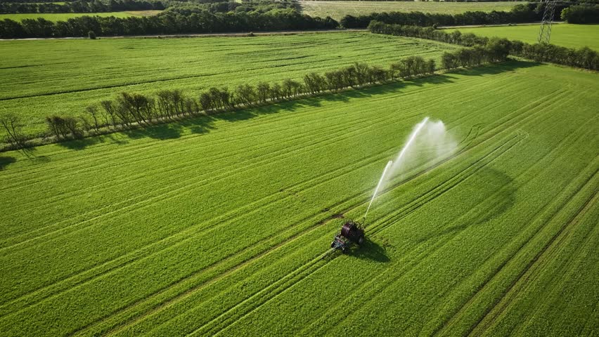 Aerial footage of mobile sprinkler irrigation system watering agricultural field. Aerial pull back shot of agricultural irrigation system watering crops.