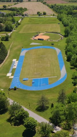 Vertical screen. Aerial view of a vibrant sports complex featuring a blue track, baseball field, and lush green fields in Brevard, North Carolina, USA