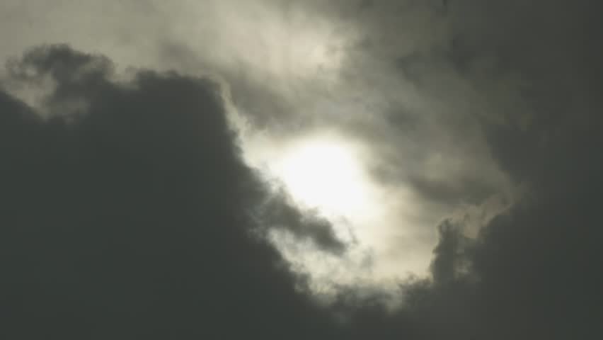 Bright sun peeking from behind a large dark storm cloud