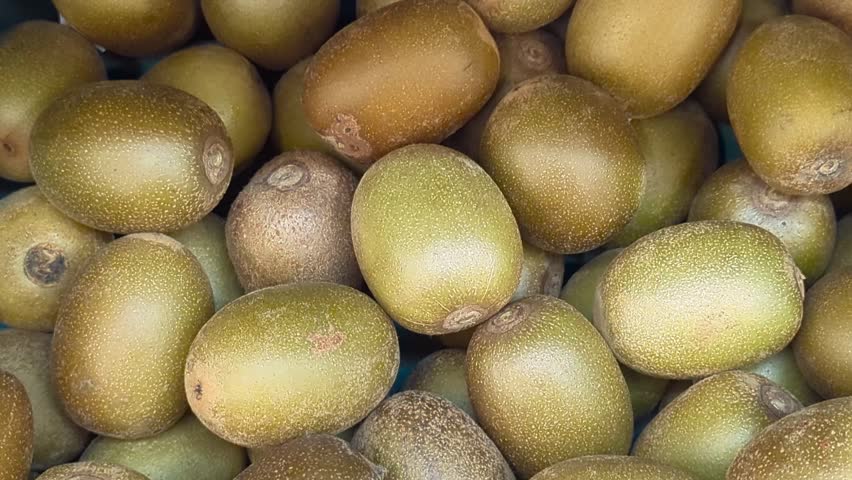 Close-up of fresh kiwi fruits stacked together in a supermarket display. The natural texture and healthy fruit concept.