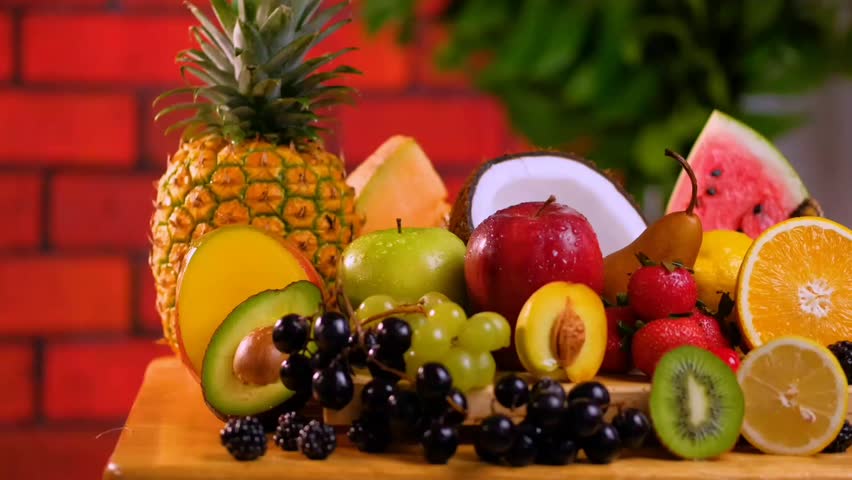 Fresh sliced fruit placed on a wooden board on a table, grapes, oranges, peaches, bananas, pineapple, watermelon, and others, as you scoop it up and down.