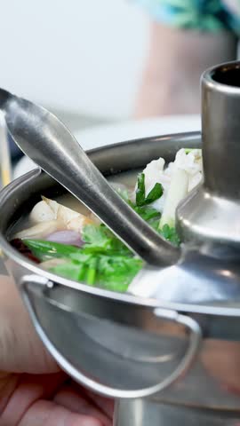 Close-up of steaming seafood soup with shrimp and cilantro served in a metal hot pot.