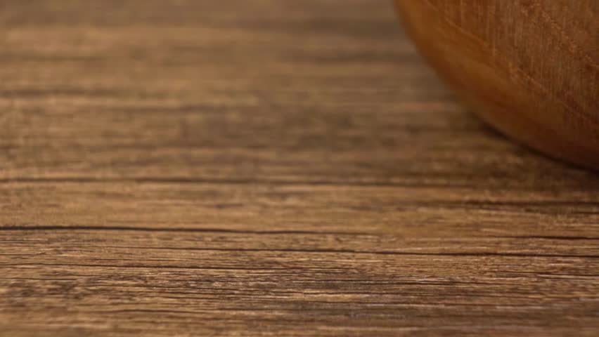 Organic brown flax seeds spilling from a rustic wooden bowl onto a wooden table