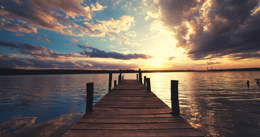 Scenic Sunset Over Wooden Fishing Jetty Pier With Sun Reflecting at Golden Hour Colors Calm Water Into Calm Lake At Dusk