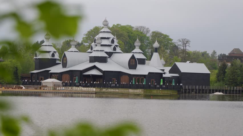 Wooden Russian-style building seen across a lake, framed by foreground leaves