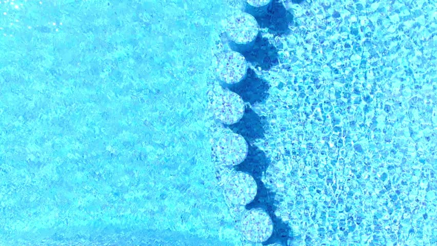 Top Down Aerial Drone view of blue swimming pool surface featuring circular entry steps, geometric patterns, and clear water textures in recreational setting.