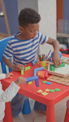 Boy playing with colorful wooden blocks, reaching with hand over a red activity table in a playroom within a building; concentration learning.