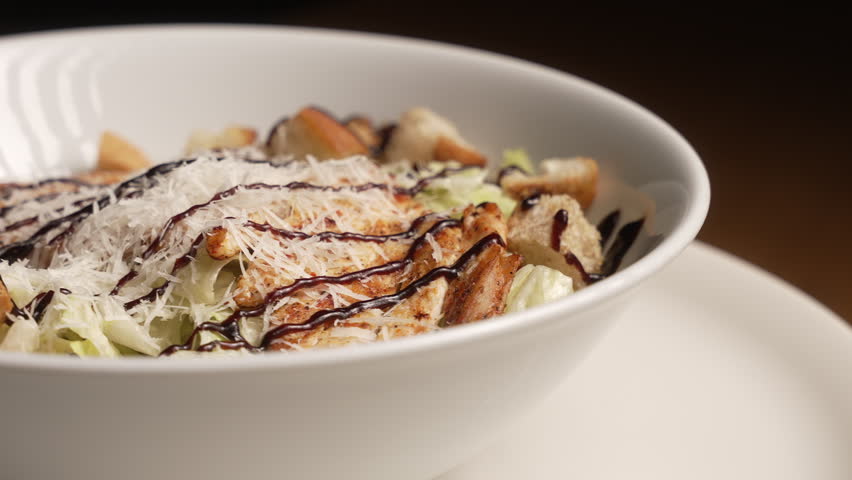 Fresh Caesar salad with grilled chicken, parmesan, and croutons rotating on a plate, fa01