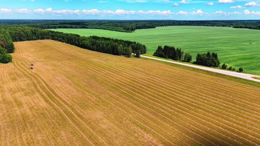 Aerial view of two tractors harvesting crops in striped fields under clear blue skies