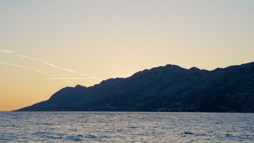 Sunset over the Adriatic Sea in Brela, Croatia, featuring the Biokovo Mountains, calm blue water and a peaceful Mediterranean coastal landscape