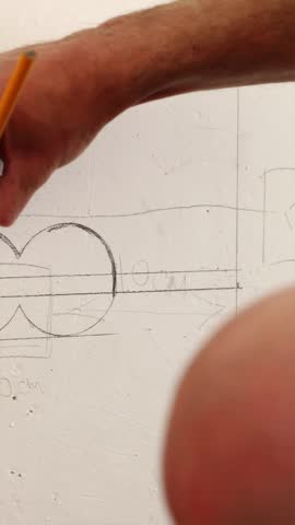 Vertical view of an electrician outlining the position for a new wall outlet using a pencil, preparing for wall drilling during home renovation.