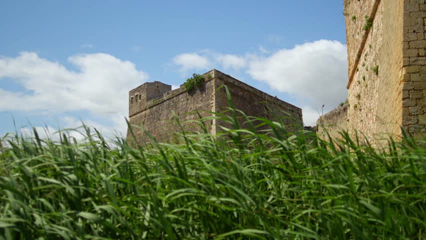 Historic limestone fortifications rise above windblown coastal vegetation in Brindisi, Apulia, Italy, showcasing centuries of Adriatic military architecture, static low angle shot.