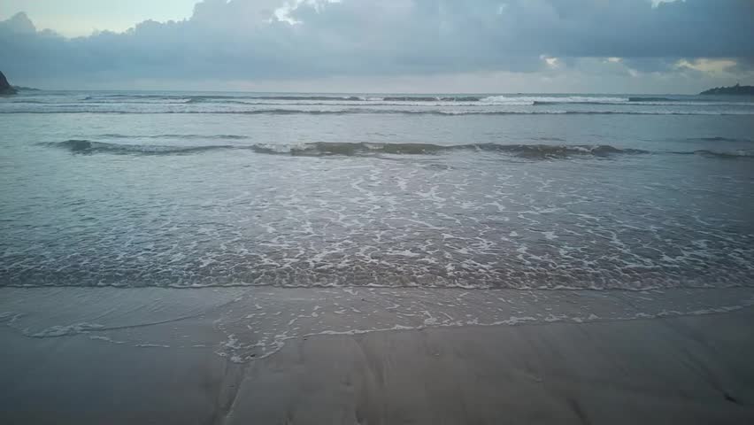 Waves wash over a sandy beach on a cloudy day with a gloomy sky