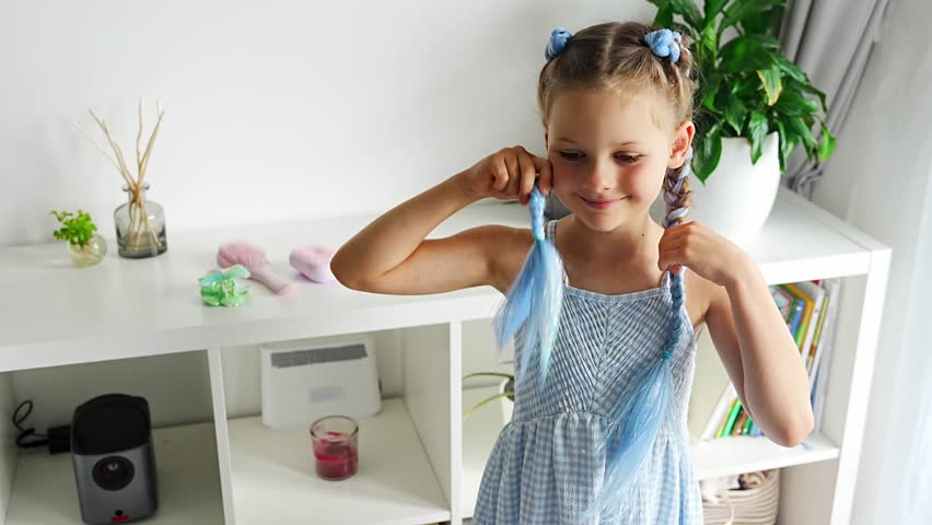 Little girl smiling and holding blue braided hair extensions like playful ears after hairstyle makeover. Childhood creativity and Generation Alpha self expression celebrate colorful beauty trends.