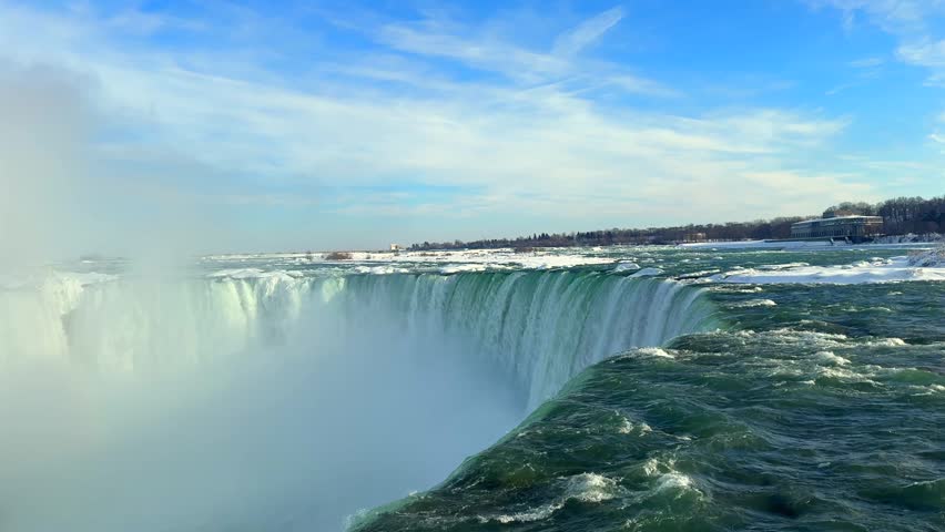 Turquoise water plunges over wide waterfall ledge creating a faint winter rainbow