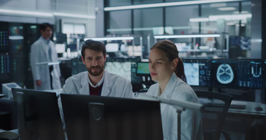 Male and Female Scientists Talk and Point at Computer Monitors Displaying Brain Scans in a Modern Medical Research Laboratory, Using Ai Technology to Advance Neurology Treatment and Drug Development.